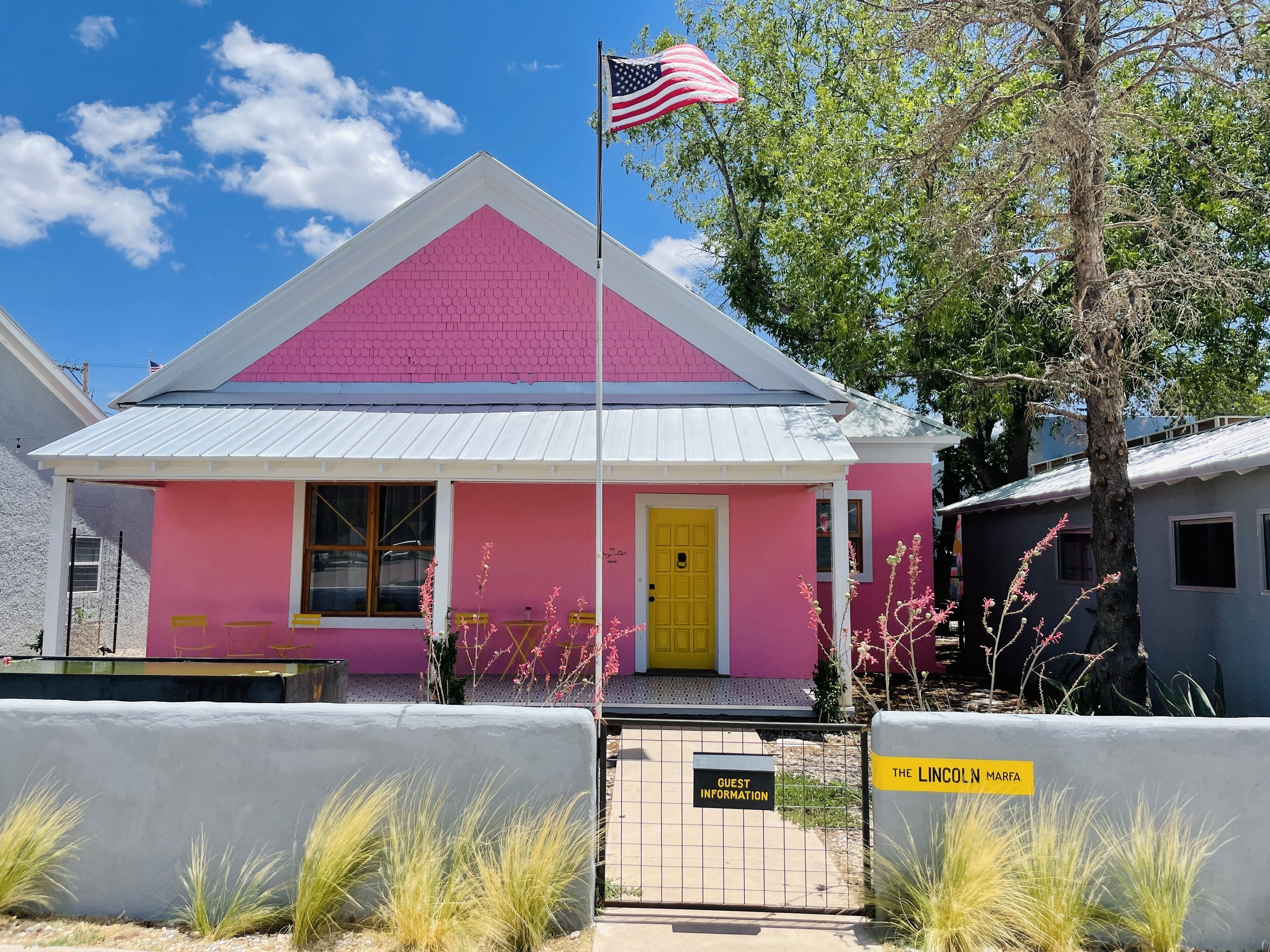 A pink building with a yellow door, an American flag, and a sign labeled "Guest Information".