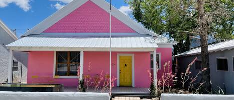 A pink building with a yellow door, an American flag, and a sign labeled "Guest Information".