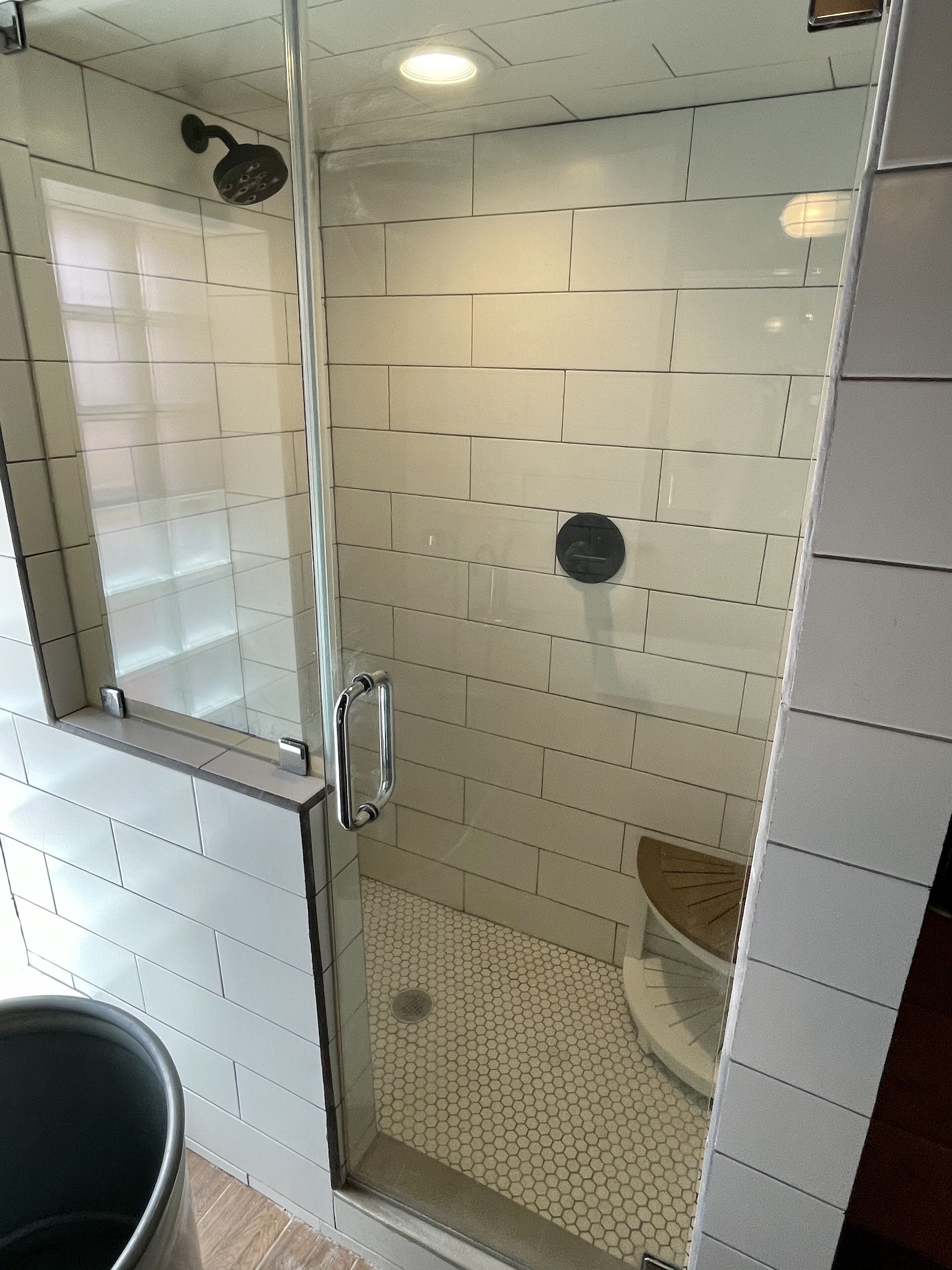 Ducha con cerramiento de vidrio, azulejos blancos y un patrón de suelo hexagonal.
