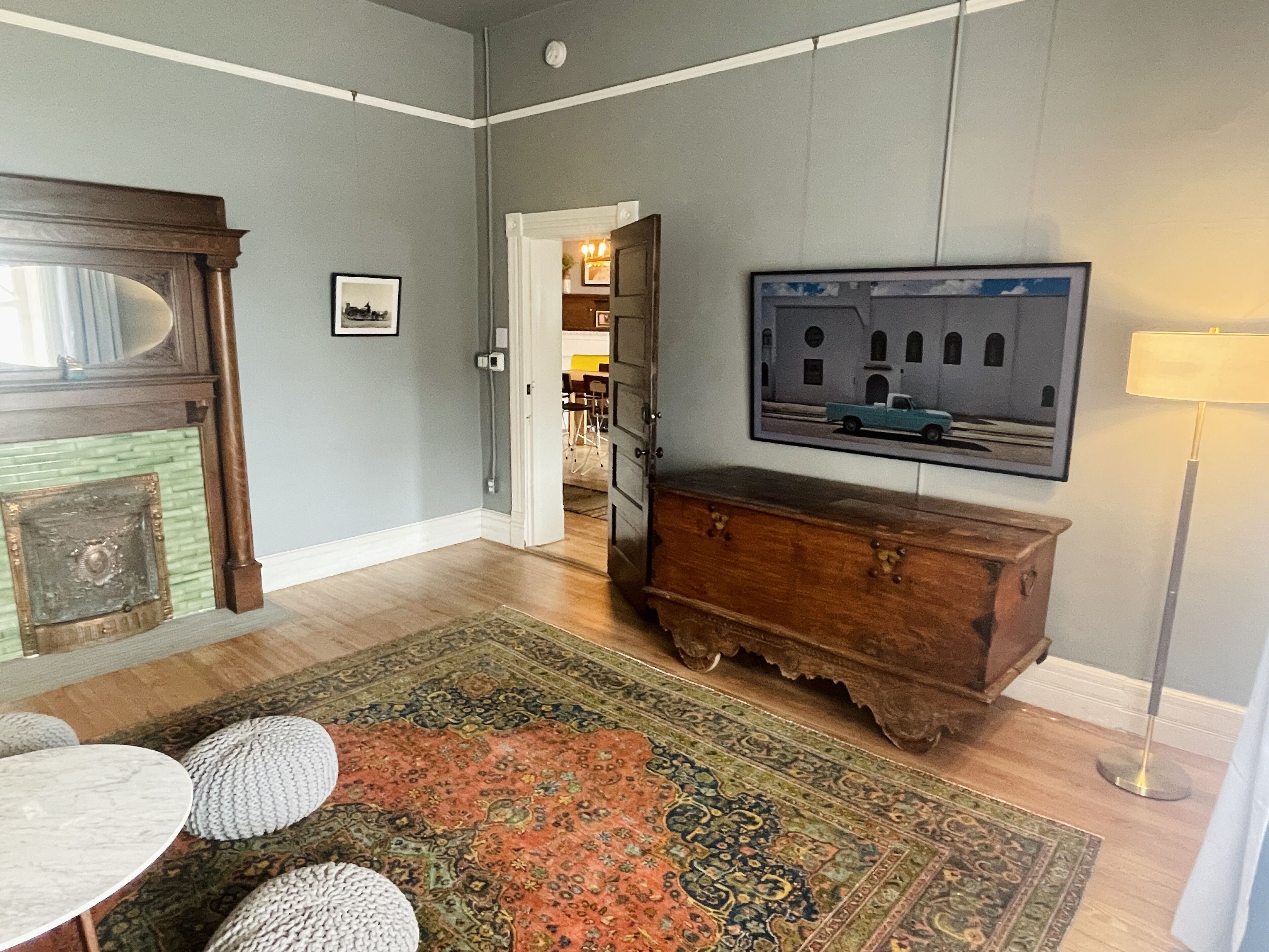 A room with a wooden dresser, a television mounted on the wall, a patterned rug, and a dining table with stools.