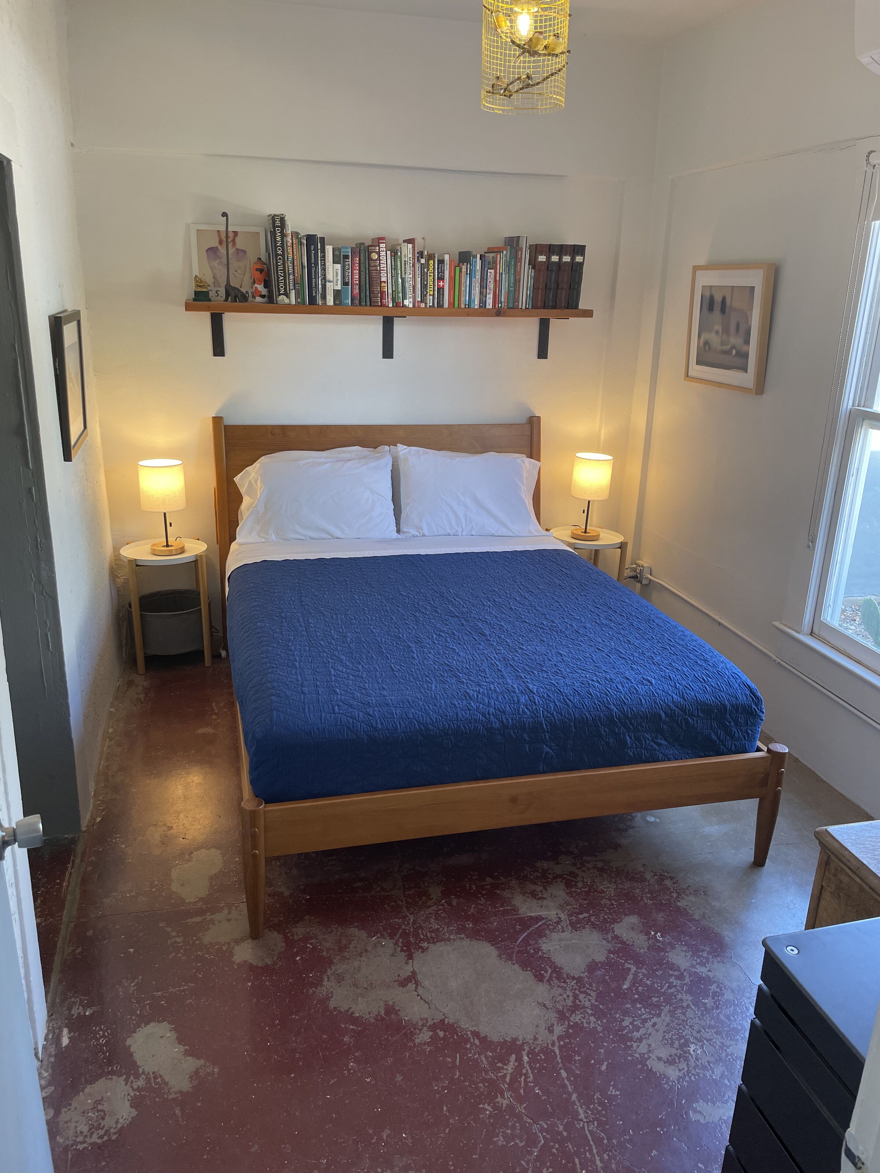 A bedroom with a wooden bed, two bedside lamps, a bookshelf, and a window.