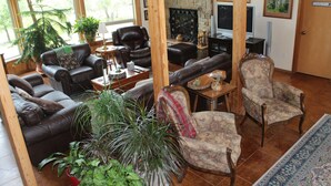 A spacious living room with leather sofas, a fireplace, and large windows. - Prow'd House Bed & Breakfast (Wimberley)