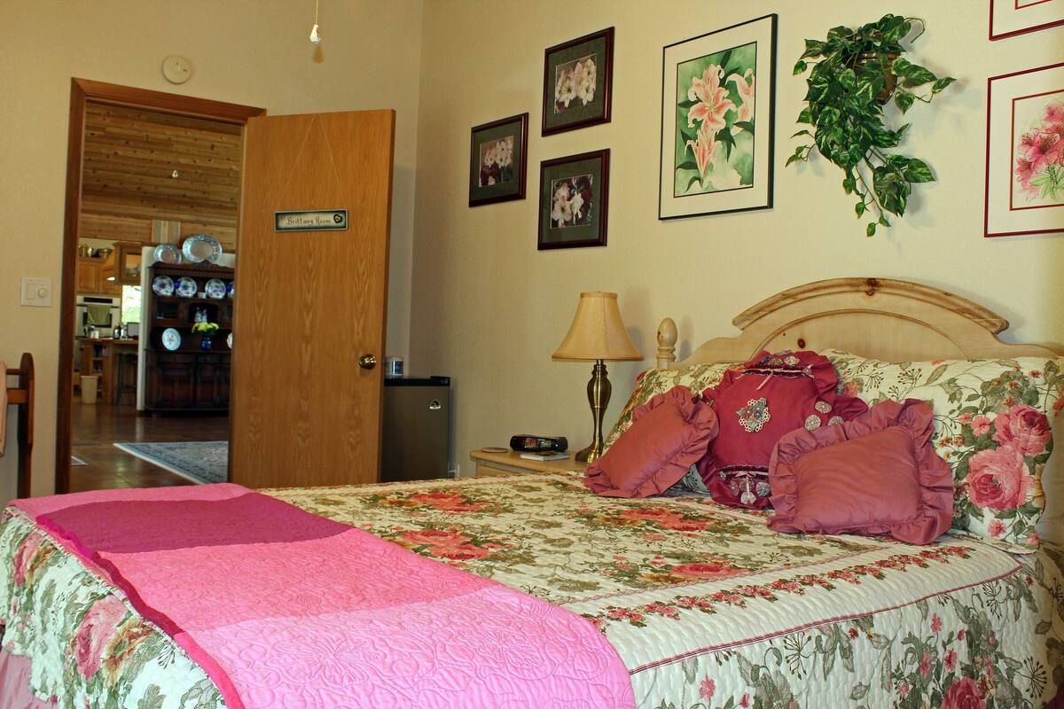 A bedroom with a bed, a nightstand, a lamp, and a wall with framed pictures.