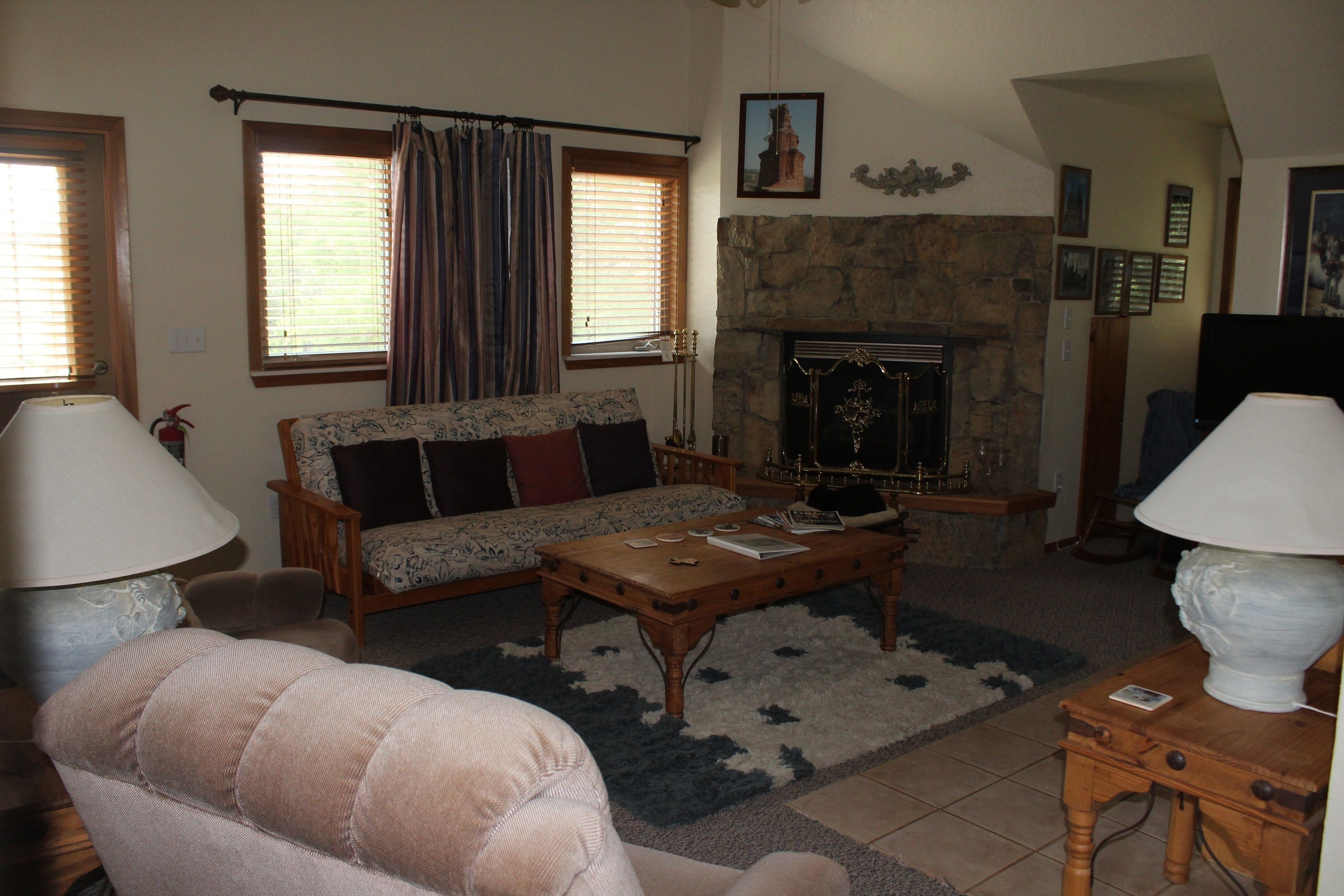 A living room with a sofa, coffee table, and lamps. There is a fireplace with a stone surround and a picture above it.