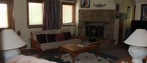 A living room with a sofa, coffee table, and lamps. There is a fireplace with a stone surround and a picture above it.