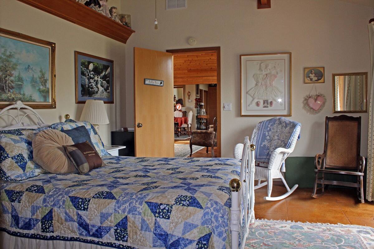 A bedroom with a bed, a rocking chair, and a chair. There is a door leading to another room.