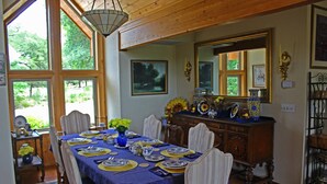 A dining room with a large table set for six, wooden chairs, a vase of flowers, and a mirror above the table. - Prow'd House Bed & Breakfast (Wimberley)