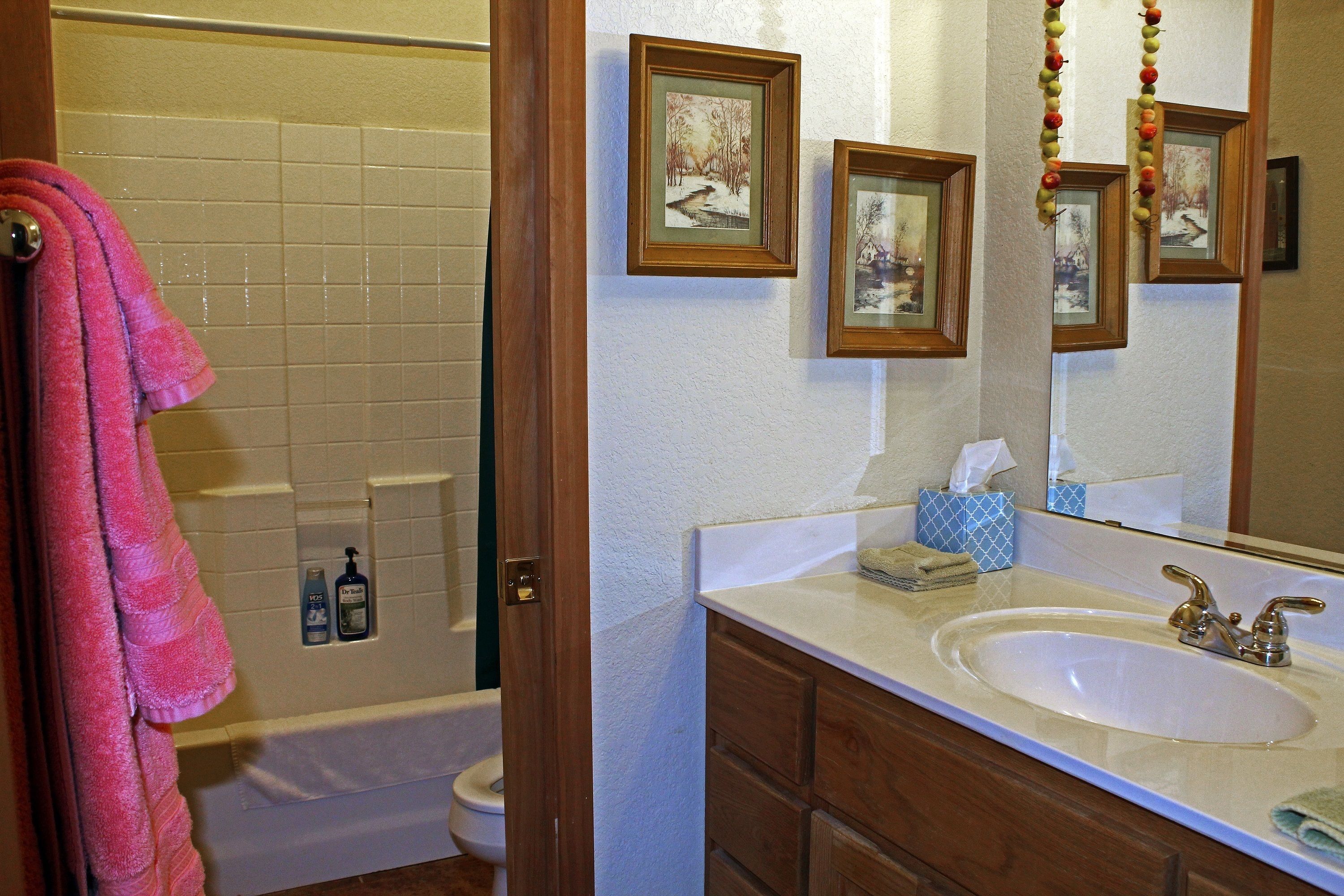 A bathroom with a white sink, wooden vanity, and a large mirror. There are framed pictures on the wall and a towel rack with a pink towel.