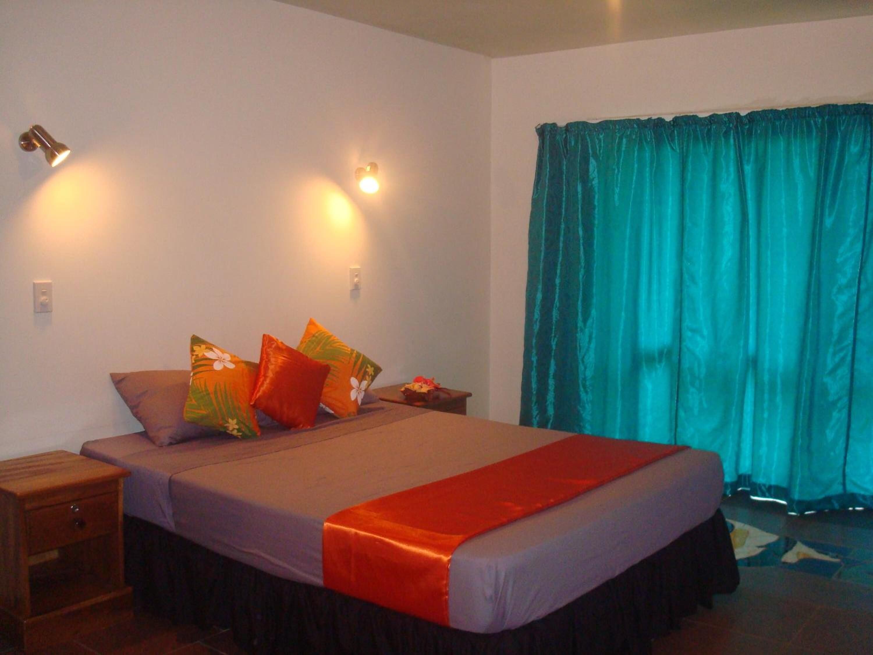 A bedroom with a bed, a nightstand, a lamp, and a window with curtains.
