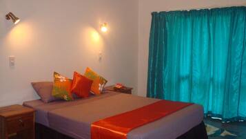 A bedroom with a bed, a nightstand, a lamp, and a window with curtains.