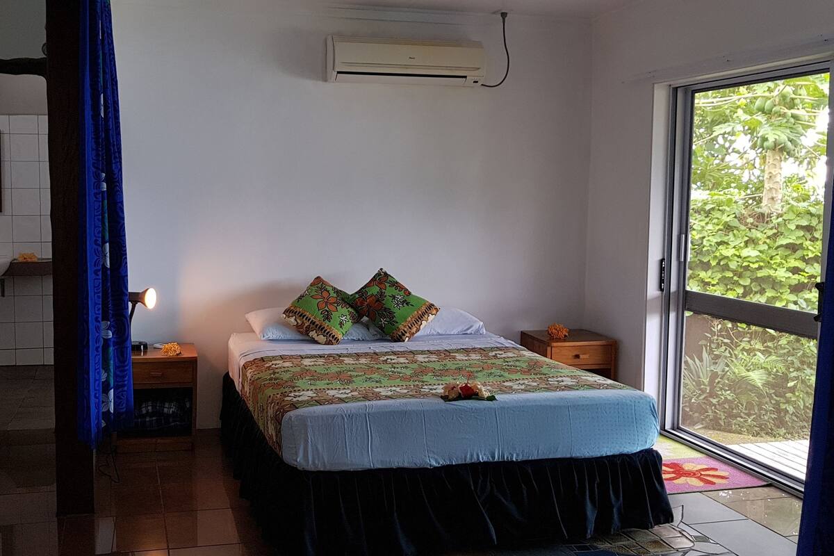 A bedroom with a bed, a nightstand, a lamp, a window, and a door.
