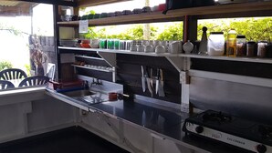 A kitchen with a gas stove, shelves with kitchenware, and a window with greenery outside. - Gecko Lodge Fiji Private Hotel (Savusavu)