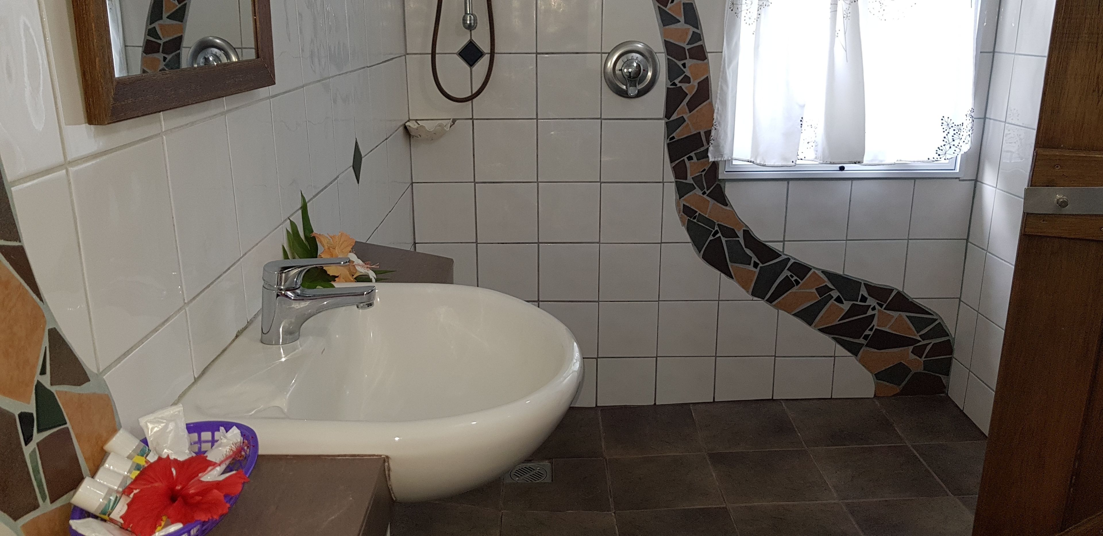 Casa de banho com lavatório branco, chuveiro e janela.