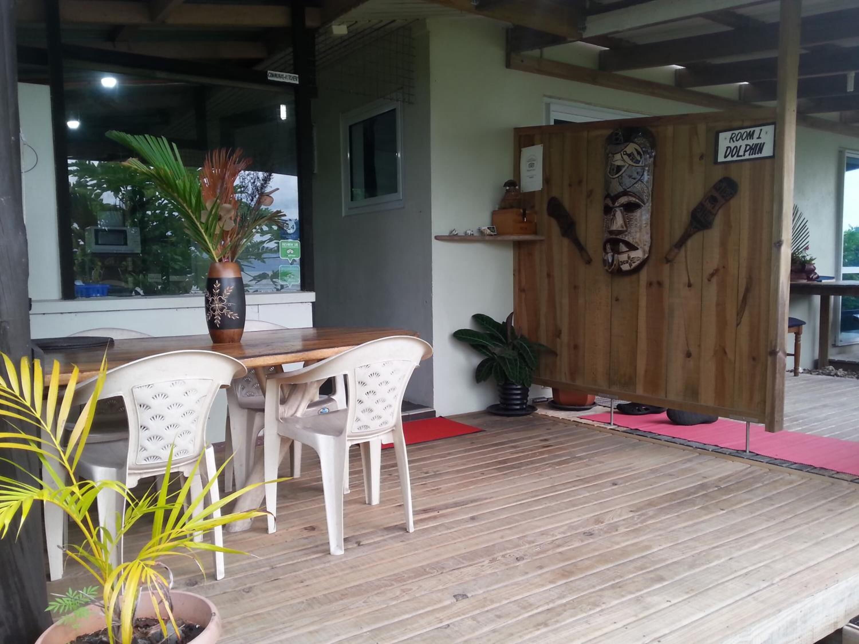 A wooden table with white chairs, a wooden partition with a dolphin mural, and potted plants.
