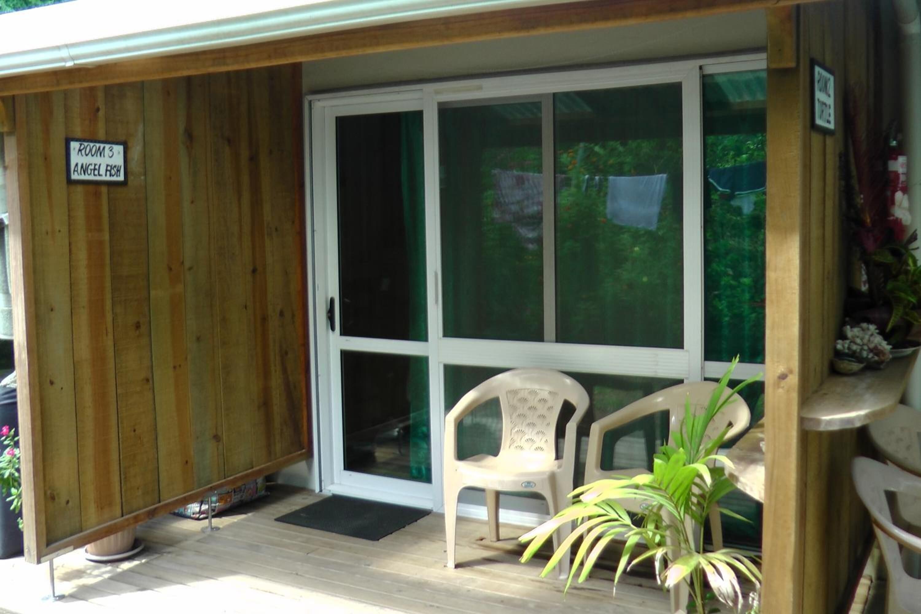 A covered porch with a sliding glass door, a plastic chair, and a potted plant.