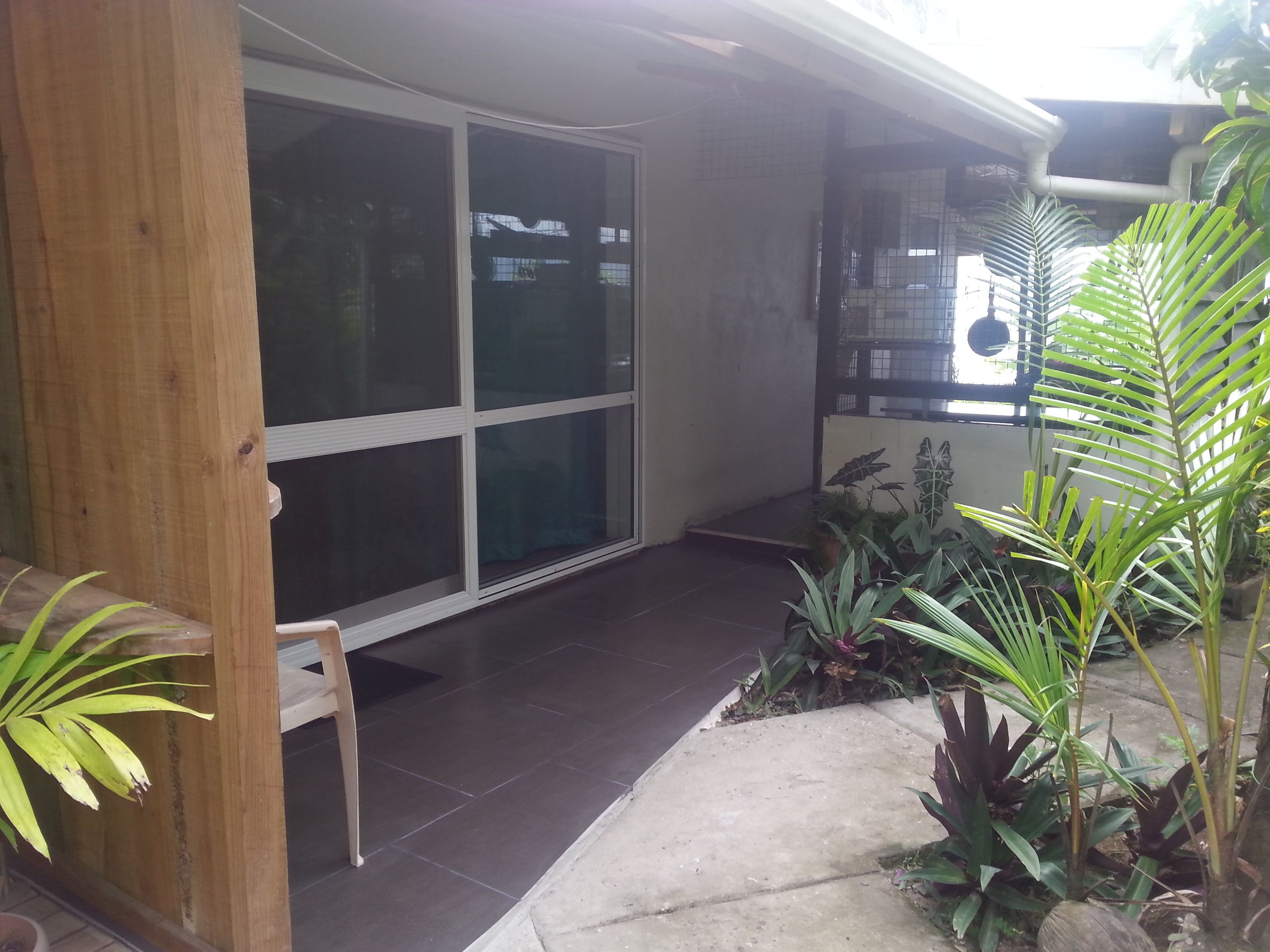 Un espacio exterior techado con una banca, puertas de vidrio y plantas en macetas.