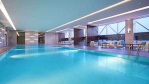 A modern indoor swimming pool with clear water, surrounded by lounge chairs and sofas, and large windows offering views. - Hyatt Regency Shanghai Jiading (Shanghai)