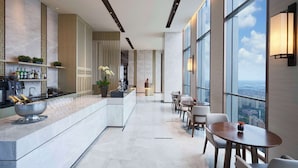 Un moderno vestíbulo de hotel con zona de bar, asientos y grandes ventanales que ofrecen vistas a la ciudad.