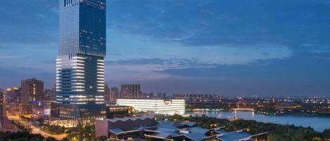 A modern high-rise hotel with a sleek, reflective facade, surrounded by lush greenery and a waterfront view.