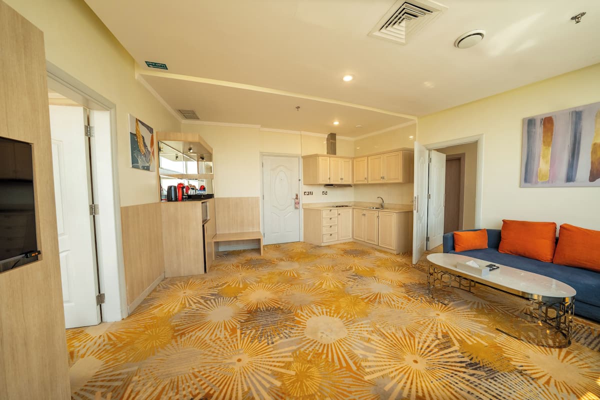 Une chambre d’hôtel moderne avec un sol à motifs, un canapé, une table basse et un coin cuisine.
