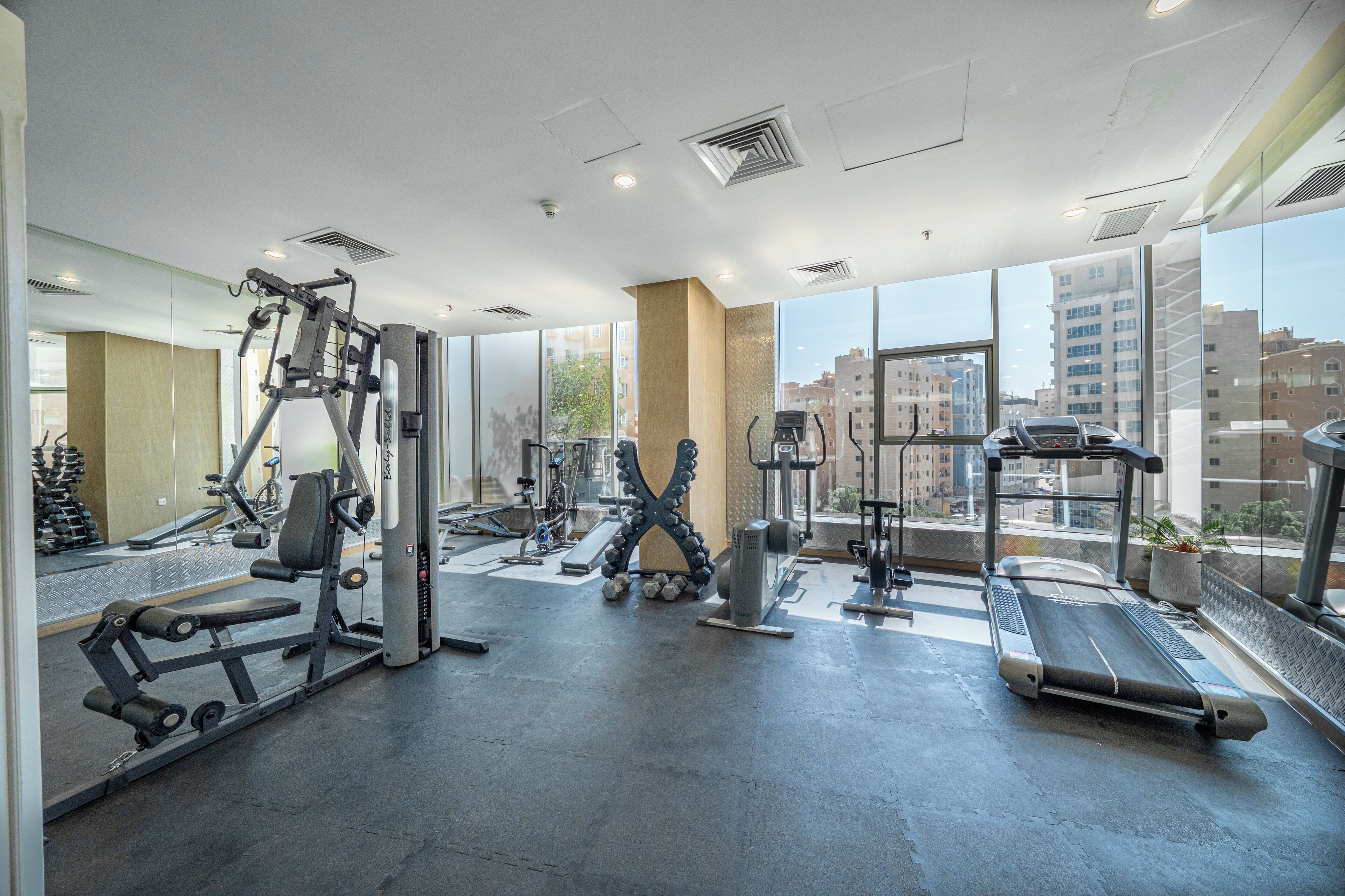 Un gimnasio moderno con diversos equipos de ejercicio, ventanas amplias y vistas a la ciudad.