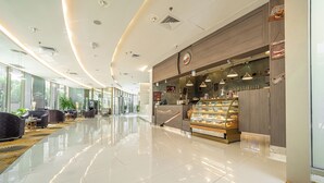 Un moderno vestíbulo de hotel con mostrador de panadería, zona de estar y ventanas amplias.