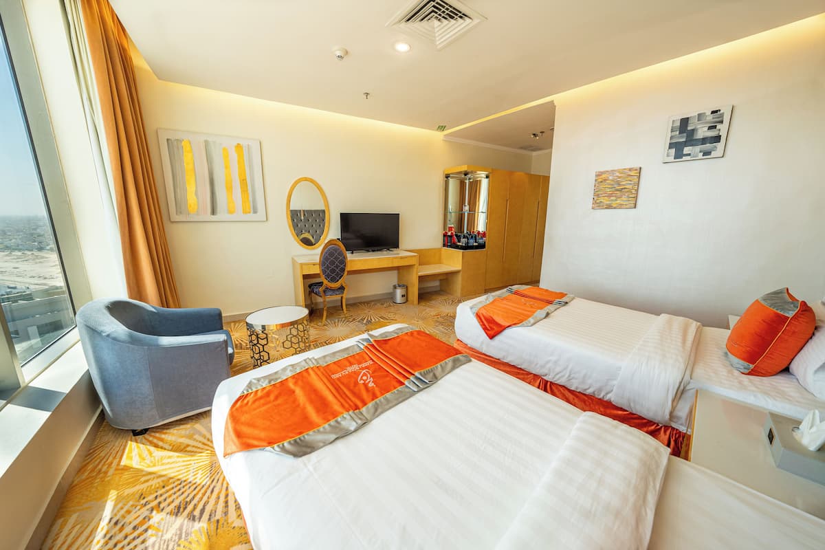 Une chambre d’hôtel avec deux lits, un bureau avec une télévision, une chaise et une grande fenêtre.