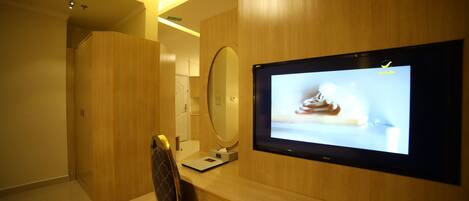 A modern hotel room with a wooden desk, a large mirror, and a flat-screen TV displaying an image of a shoe.