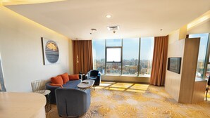 Una habitación de hotel moderna con un ventanal grande, un sofá, una silla y una mesita.