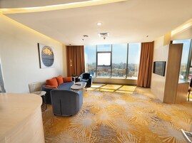 Una habitación de hotel moderna con un ventanal grande, un sofá, una silla y una mesita.