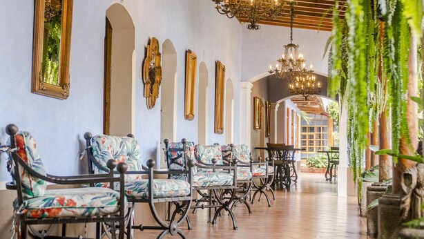 Un pasillo amplio con sillones estampados, un candelabro y espejos en la pared.