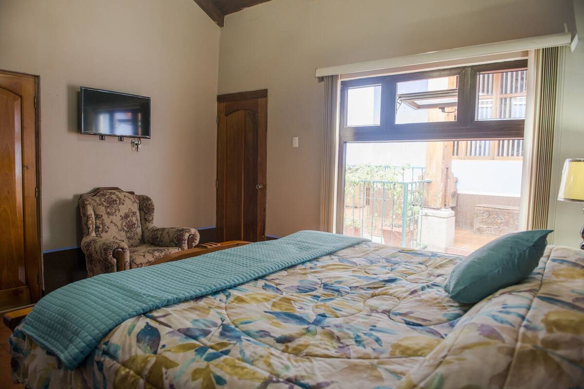 A bedroom with a bed, a chair, a television, and a sliding glass door to an outdoor area.