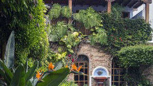 Un patio con piso de piedra, una fuente y abundante vegetación.