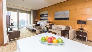 Una habitación de hotel con cama, sofá, mesa de comedor con fruta y vistas a la ciudad.