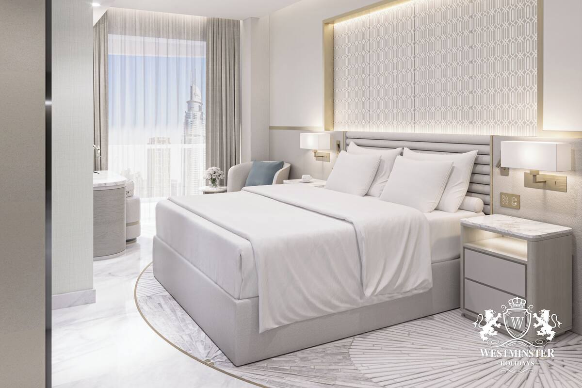 A modern hotel room with a large bed, bedside tables, a nightstand, a wall-mounted light fixture, and a view of the city skyline.