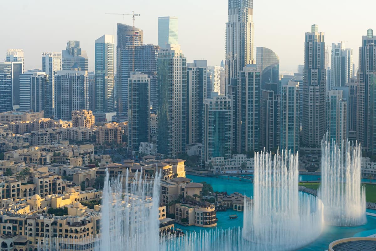 A cityscape with tall buildings and a central water feature with fountains.