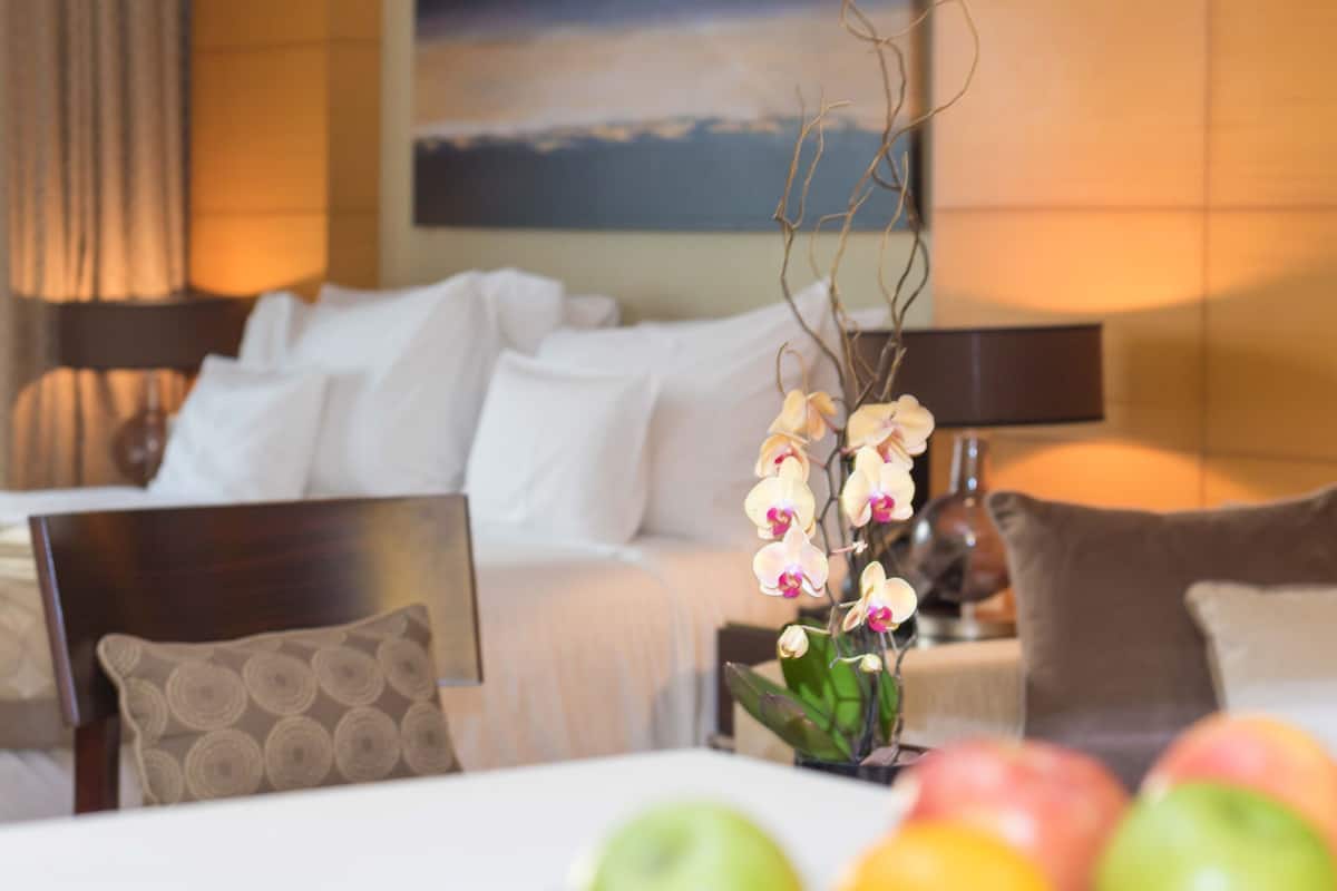 A hotel room with a bed, pillows, a vase with flowers, and apples on the table.