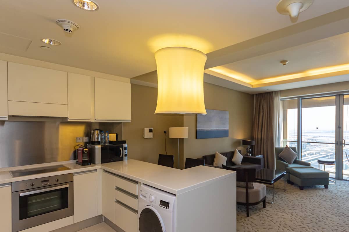 A modern hotel room with a kitchen area, a washing machine, a flat-screen TV, and a seating area with a view.