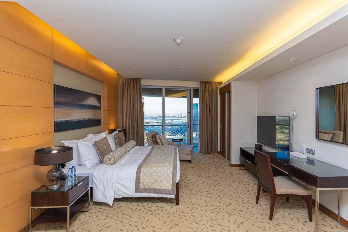 A hotel room with a bed, a desk, a TV, and a view of the city.