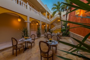 Um pátio de hotel com várias mesas e cadeiras de jantar, uma escadaria e uma palmeira.