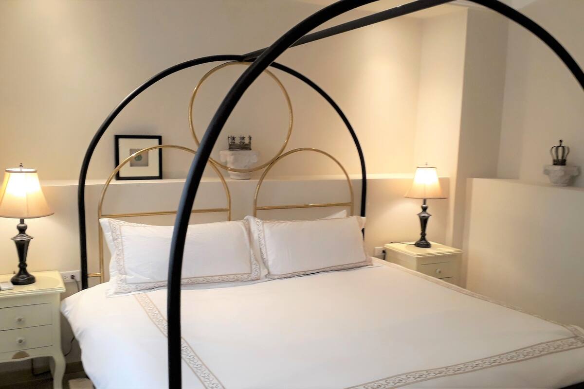 A bed with a canopy, two bedside tables with lamps, a nightstand, and a framed picture on the wall.