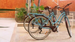 Een turquoise fiets met mandje en bruine zitting geparkeerd naast een witte stoel onder een parasol.