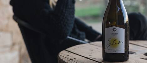 Una botella de vino Solane sobre una mesa con una persona sosteniendo una copa.