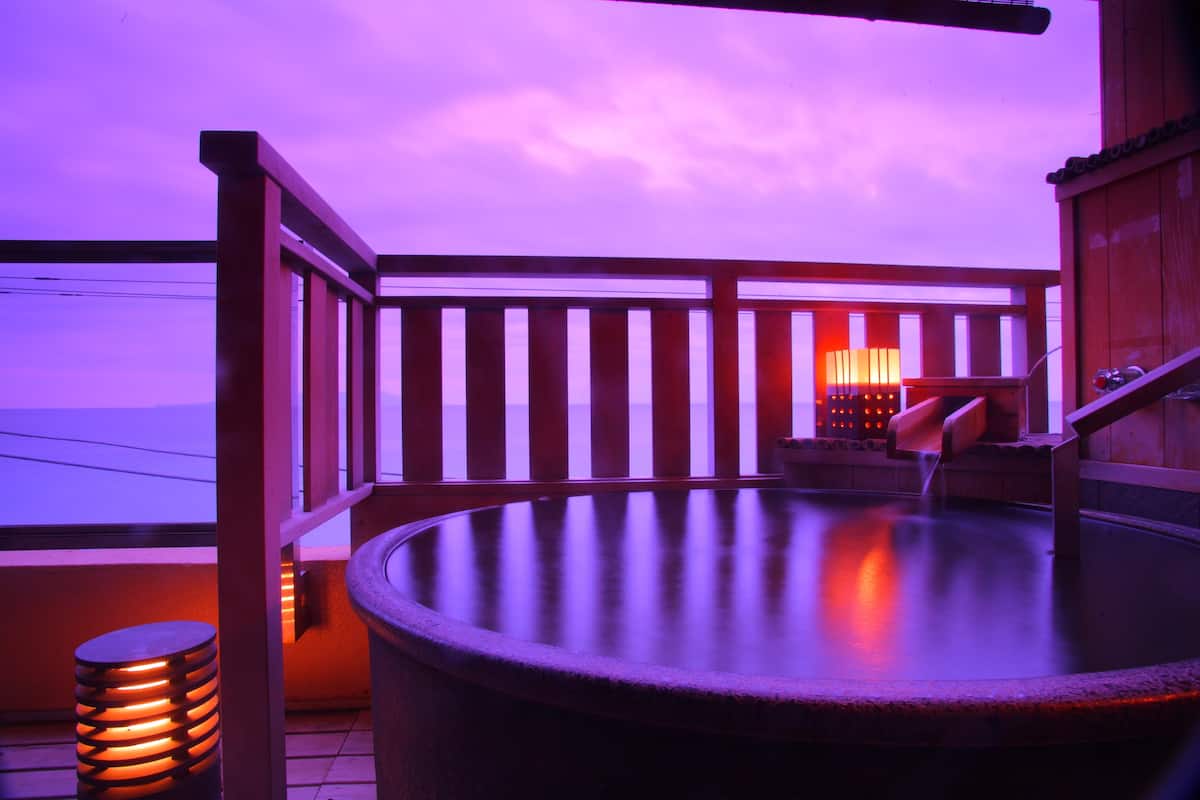 A hot tub on a balcony with a wooden railing, a chair, and a small table.
