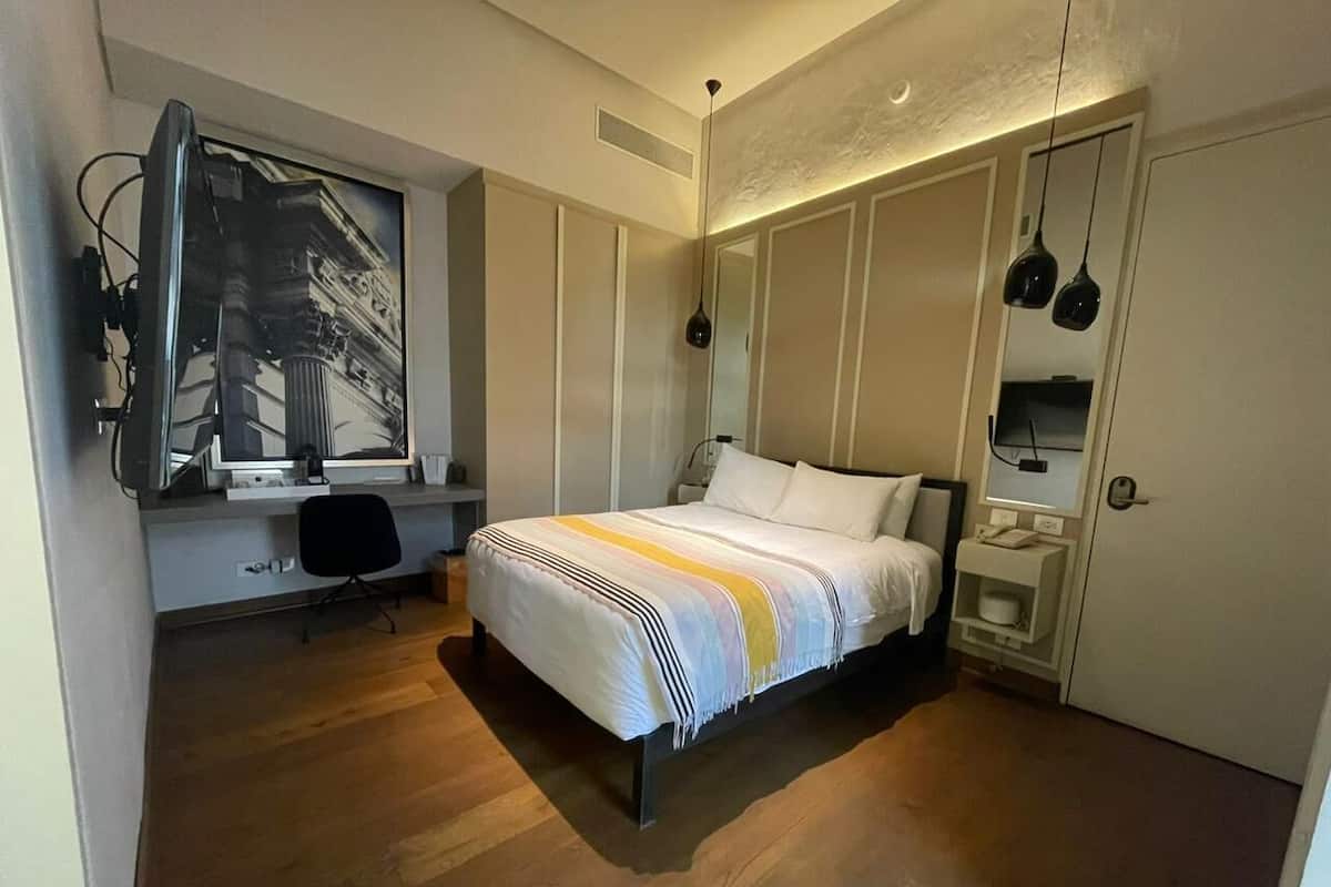 Una camera da letto con un letto, una scrivania con un computer, una sedia, un armadio e una lampada a sospensione.