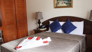 Una cama bien hecha con una colcha estampada, dos almohadas, una lámpara de noche y un teléfono en la mesita.
