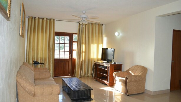 Una sala de estar con sofá, sillón, mueble para televisión y cortinas.