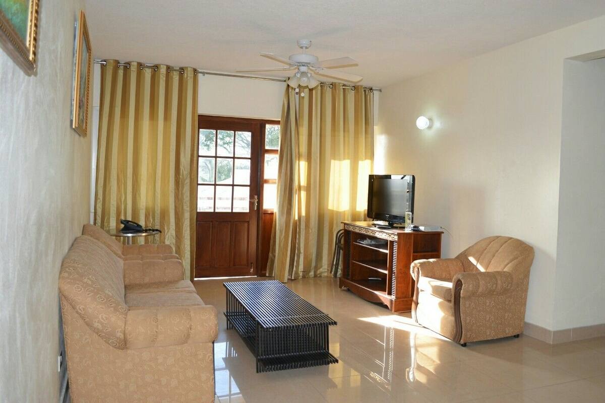 A living room with a sofa, armchair, TV stand, and curtains.