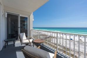 A balcony with a view of the beach, a glass door, and a seating area with a table and chairs. - Inn at Crystal Beach 410 * Gulf Front with Beach Chair Set. Onsite dining! (Destin)