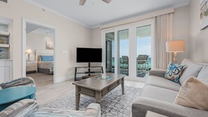Ein großzügiges Wohnzimmer mit Flachbildfernseher, Couchtisch und Sofa. Ein Balkon bietet Blick ins Freie.